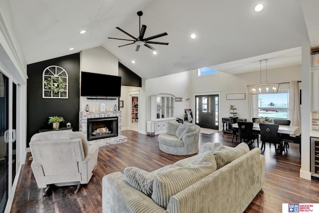 living room featuring high vaulted ceiling, ceiling fan with notable chandelier, a brick fireplace, dark hardwood / wood-style floors, and beverage cooler