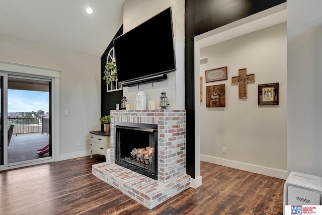 living room with dark wood-type flooring, vaulted ceiling, and a brick fireplace