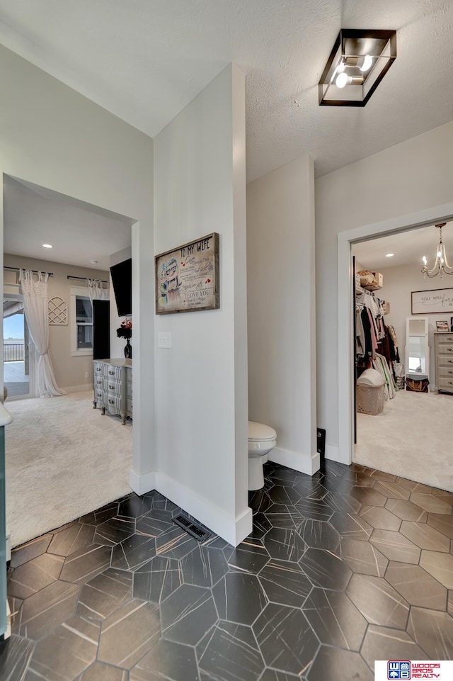 hall with an inviting chandelier and dark colored carpet