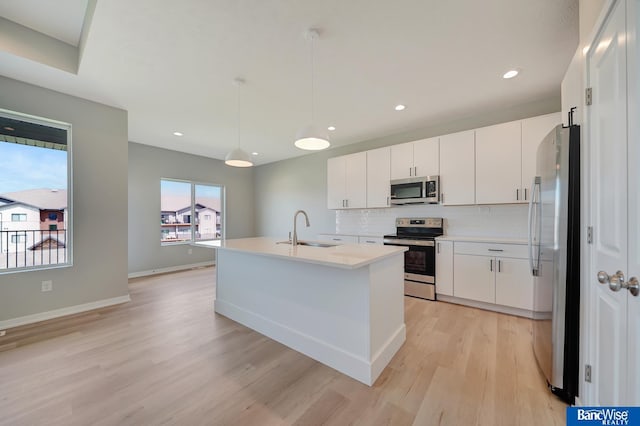 kitchen featuring sink, light hardwood / wood-style floors, decorative light fixtures, white cabinets, and appliances with stainless steel finishes