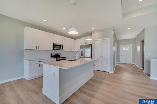 kitchen with white cabinets, stainless steel appliances, hanging light fixtures, and a center island with sink