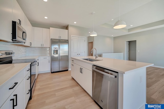 kitchen with stainless steel appliances, sink, a center island with sink, white cabinetry, and hanging light fixtures