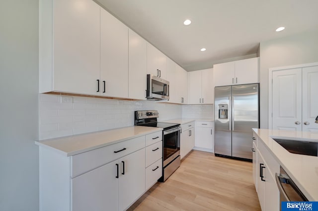 kitchen with sink, light hardwood / wood-style flooring, decorative backsplash, white cabinetry, and stainless steel appliances