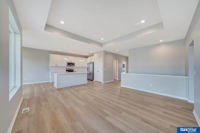 unfurnished living room featuring a raised ceiling and light wood-type flooring