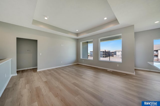 empty room featuring a tray ceiling and light hardwood / wood-style flooring