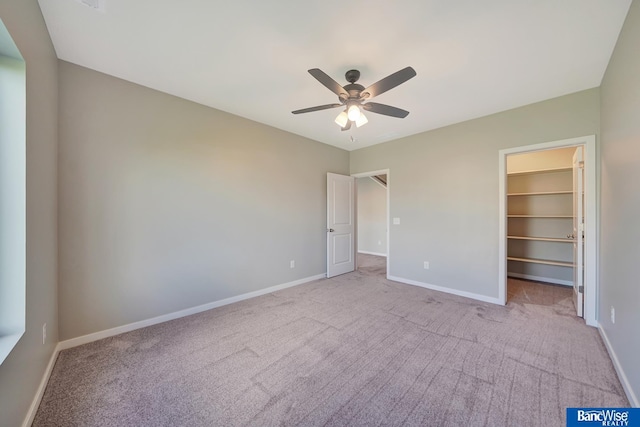 unfurnished bedroom featuring light carpet, a walk in closet, a closet, and ceiling fan