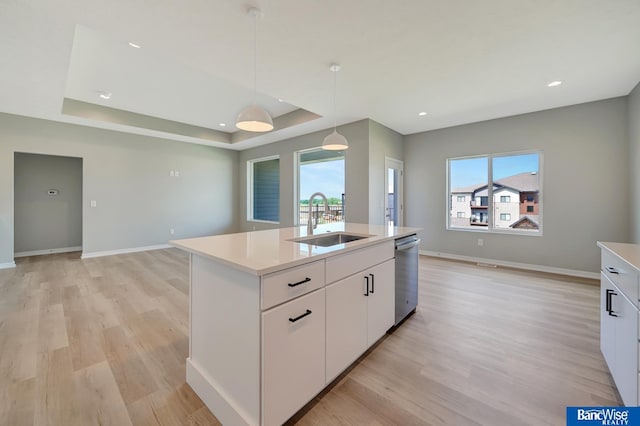 kitchen featuring white cabinetry, sink, light hardwood / wood-style floors, decorative light fixtures, and a center island with sink