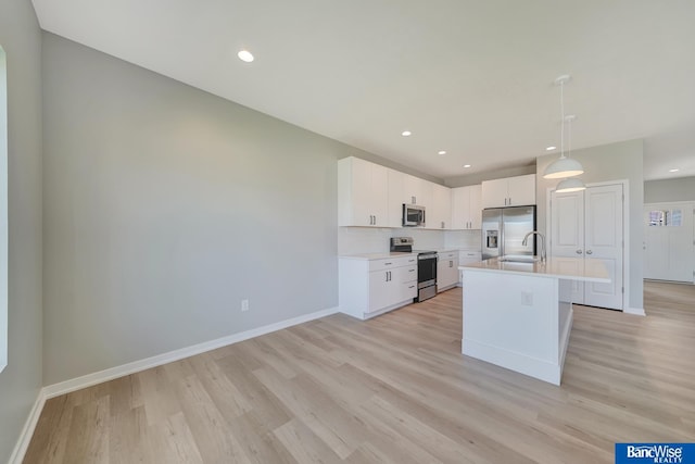 kitchen featuring a kitchen island with sink, white cabinets, light hardwood / wood-style flooring, appliances with stainless steel finishes, and decorative light fixtures