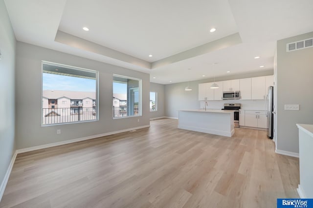 unfurnished living room with a tray ceiling, sink, and light wood-type flooring