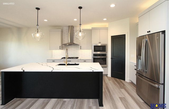 kitchen featuring stainless steel appliances, hanging light fixtures, a kitchen island with sink, white cabinetry, and wall chimney exhaust hood