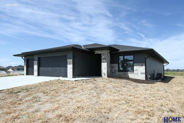 prairie-style home featuring a garage, stone siding, a shingled roof, and central air condition unit