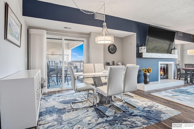 dining area with hardwood / wood-style floors, a textured ceiling, and a brick fireplace