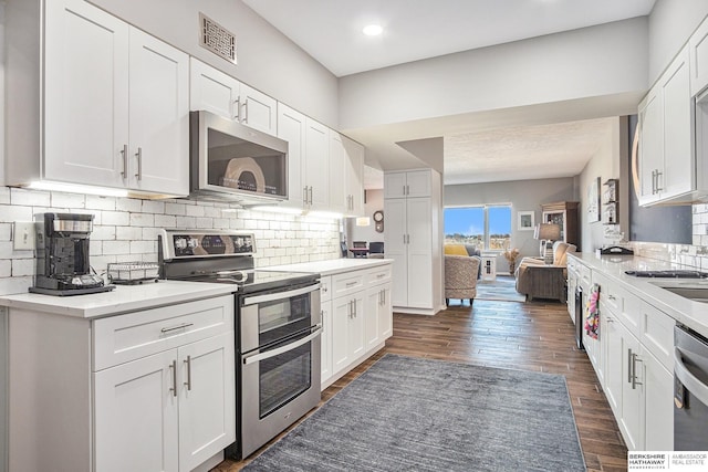 kitchen with dark hardwood / wood-style flooring, white cabinetry, backsplash, and appliances with stainless steel finishes