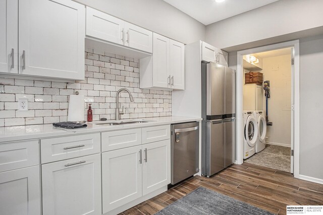 kitchen with washer and clothes dryer, white cabinets, sink, dark hardwood / wood-style floors, and stainless steel appliances