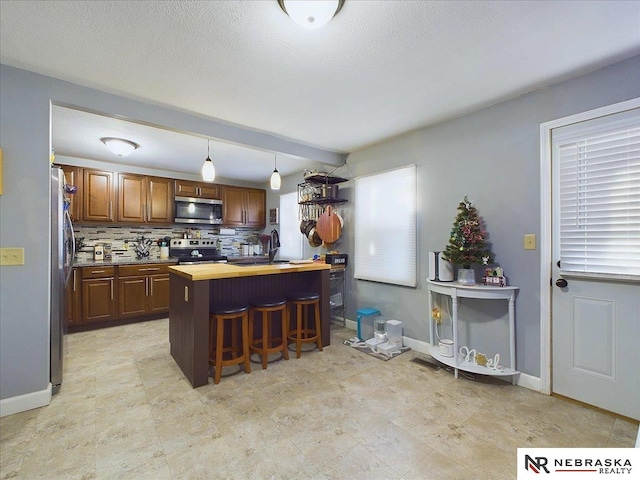 kitchen with a wealth of natural light, decorative backsplash, stainless steel appliances, and hanging light fixtures