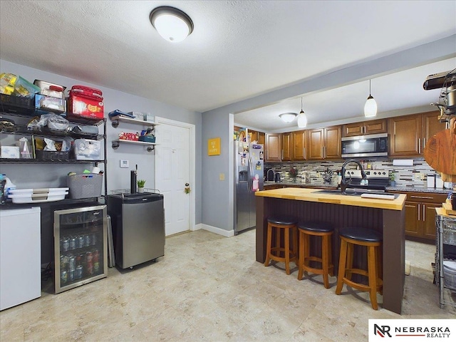 kitchen with wooden counters, appliances with stainless steel finishes, decorative backsplash, beverage cooler, and sink