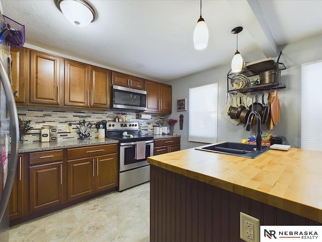 kitchen with pendant lighting, sink, tasteful backsplash, butcher block counters, and stainless steel appliances