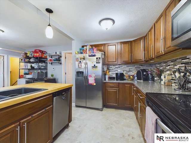 kitchen featuring backsplash, sink, hanging light fixtures, a textured ceiling, and appliances with stainless steel finishes