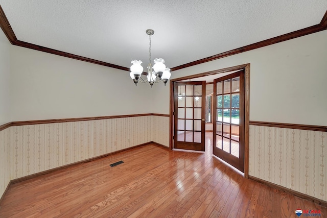 unfurnished room with french doors, a textured ceiling, hardwood / wood-style flooring, and a notable chandelier