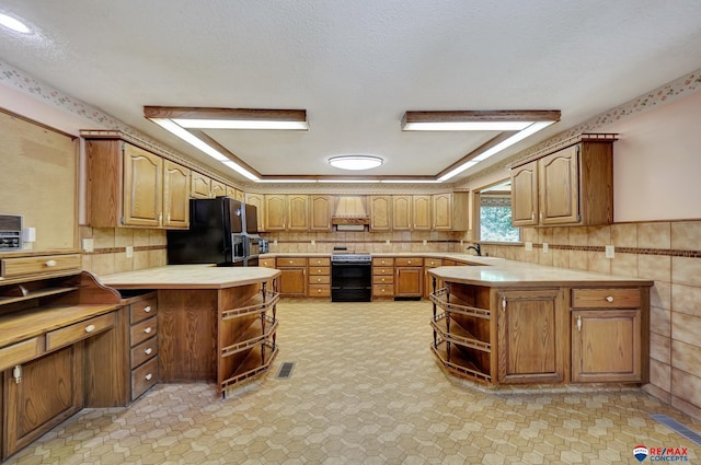 kitchen featuring kitchen peninsula, black fridge, a textured ceiling, sink, and range