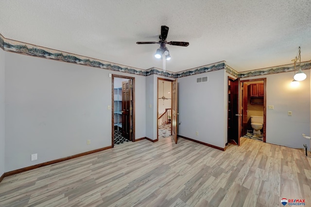 interior space with a textured ceiling, ensuite bathroom, a spacious closet, and light hardwood / wood-style flooring