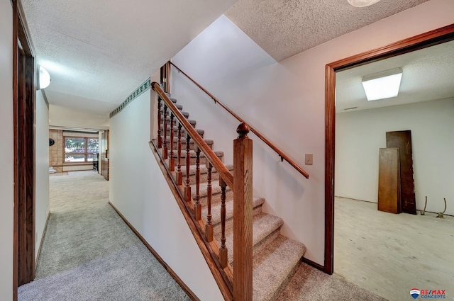 staircase with lofted ceiling, carpet floors, and a textured ceiling