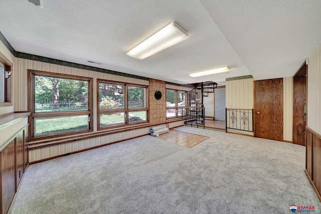 carpeted spare room featuring a textured ceiling, wooden walls, and a baseboard heating unit