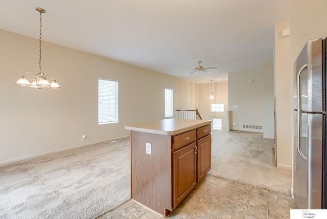 kitchen featuring pendant lighting, ceiling fan with notable chandelier, stainless steel fridge, a kitchen island, and light colored carpet