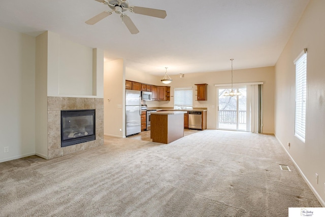 kitchen featuring hanging light fixtures, stainless steel appliances, light colored carpet, a fireplace, and a kitchen island