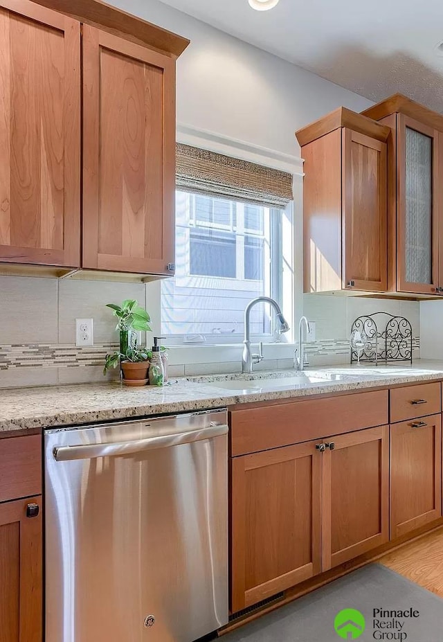 kitchen with light stone countertops, sink, tasteful backsplash, stainless steel dishwasher, and light wood-type flooring