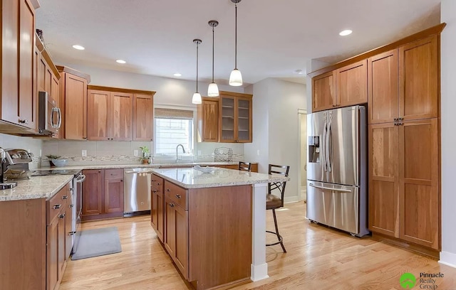 kitchen with appliances with stainless steel finishes, a center island, light hardwood / wood-style flooring, and hanging light fixtures