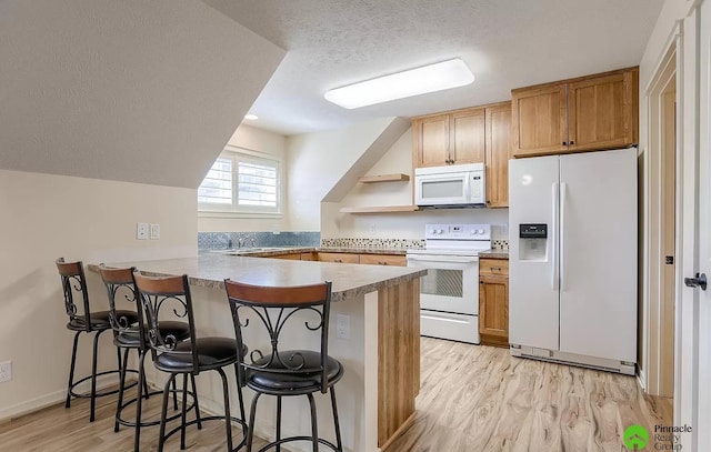 kitchen featuring kitchen peninsula, light hardwood / wood-style floors, a textured ceiling, white appliances, and a kitchen bar