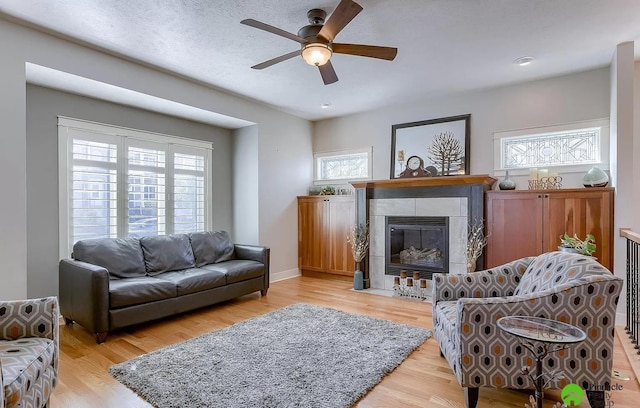 living room with plenty of natural light, ceiling fan, light wood-type flooring, and a tiled fireplace