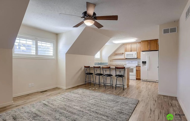 kitchen featuring white appliances, light hardwood / wood-style flooring, a textured ceiling, a kitchen bar, and kitchen peninsula