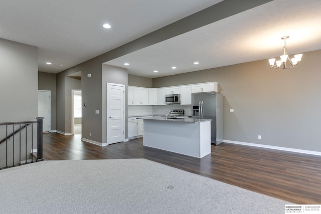 kitchen featuring dark wood-type flooring, hanging light fixtures, an island with sink, appliances with stainless steel finishes, and white cabinetry