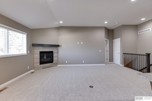 unfurnished living room with a tiled fireplace, light carpet, and lofted ceiling