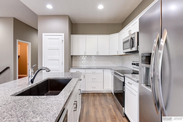 kitchen with light stone counters, stainless steel appliances, sink, hardwood / wood-style floors, and white cabinetry