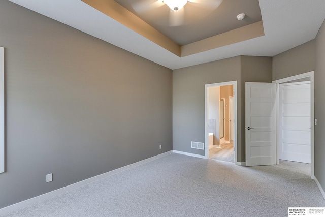 unfurnished bedroom with light colored carpet, a raised ceiling, and ceiling fan