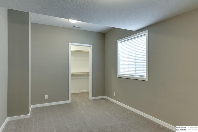 unfurnished bedroom featuring light carpet, a textured ceiling, a spacious closet, and a closet