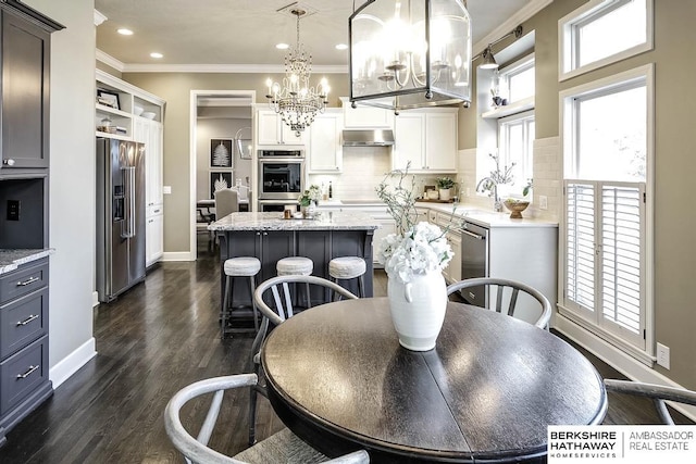 kitchen featuring dark wood-type flooring, white cabinets, hanging light fixtures, appliances with stainless steel finishes, and a kitchen island