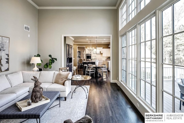 living room featuring crown molding, a towering ceiling, dark wood-type flooring, and an inviting chandelier