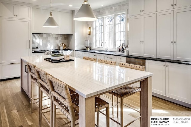 kitchen featuring white cabinetry, a center island, light hardwood / wood-style floors, decorative light fixtures, and a breakfast bar