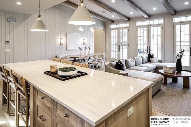 kitchen featuring beamed ceiling, pendant lighting, french doors, and wood walls