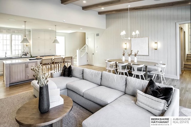 living room featuring sink, beamed ceiling, a chandelier, wooden walls, and light wood-type flooring