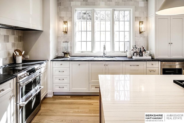 kitchen with white cabinets, backsplash, stainless steel range, and light hardwood / wood-style flooring