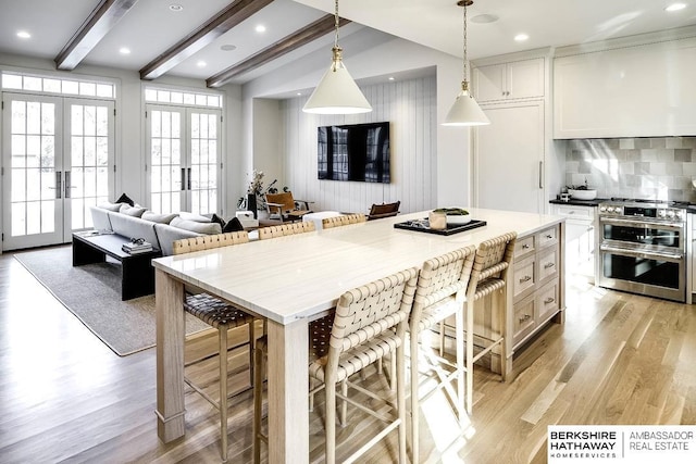 kitchen featuring french doors, a kitchen breakfast bar, beam ceiling, range with two ovens, and white cabinets