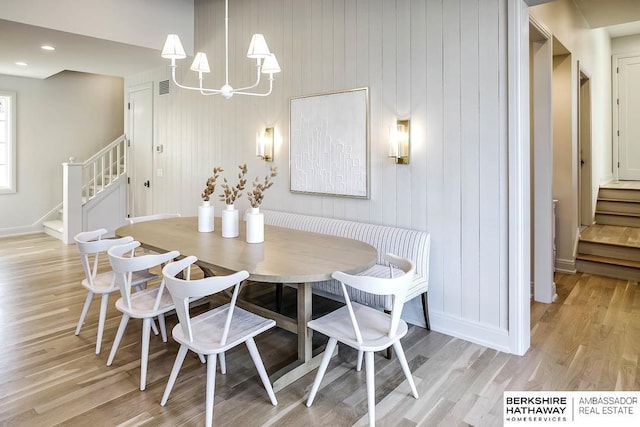 dining area with wood walls, breakfast area, light hardwood / wood-style floors, and an inviting chandelier