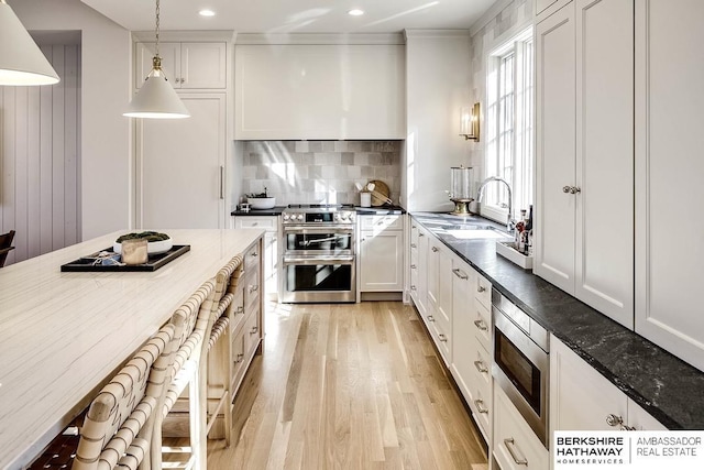 kitchen with sink, pendant lighting, light hardwood / wood-style floors, white cabinets, and appliances with stainless steel finishes