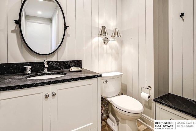 bathroom with hardwood / wood-style floors, vanity, toilet, and wooden walls