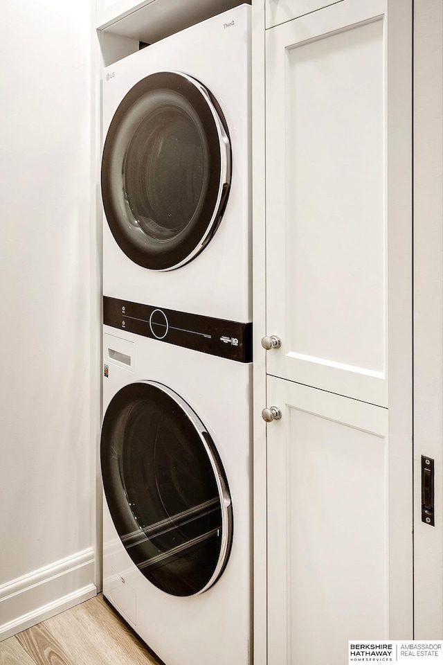 clothes washing area featuring cabinets, light wood-type flooring, and stacked washer / drying machine